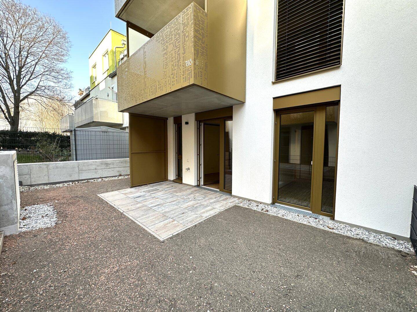 Sonniger Terrassenbereich im Freien, direkt am Gebäude gelegen, mit Kiesumrandung.