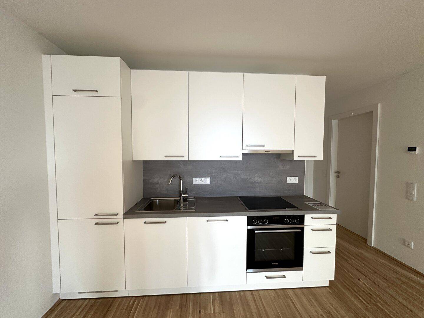 Moderne Küchenzeile mit weißen Schränken, integriertem Backofen und Induktionskochfeld.