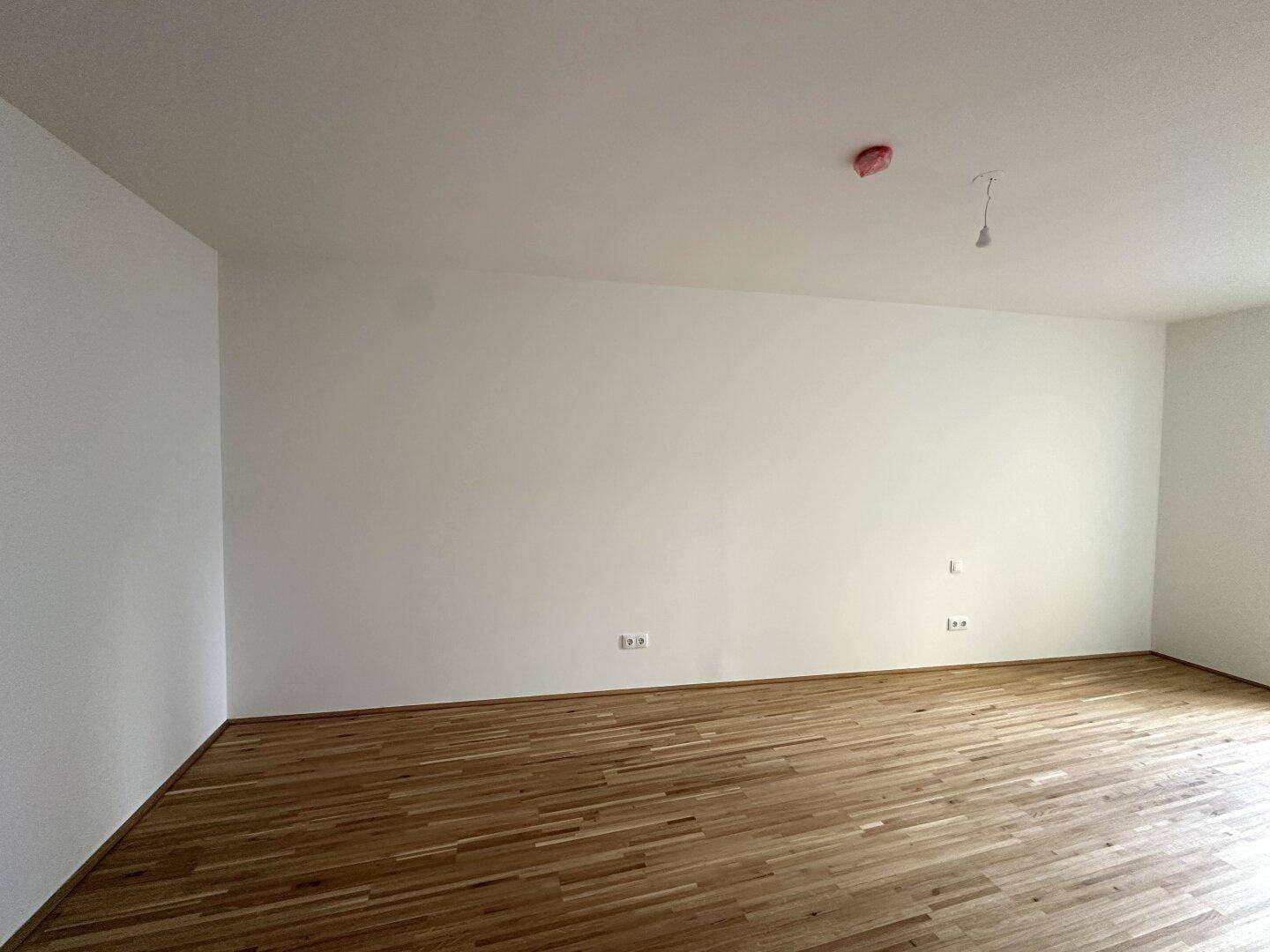 Heller, leerer Wohnbereich mit Parkettboden und weißen Wänden, bereit zur individuellen Gestaltung.
