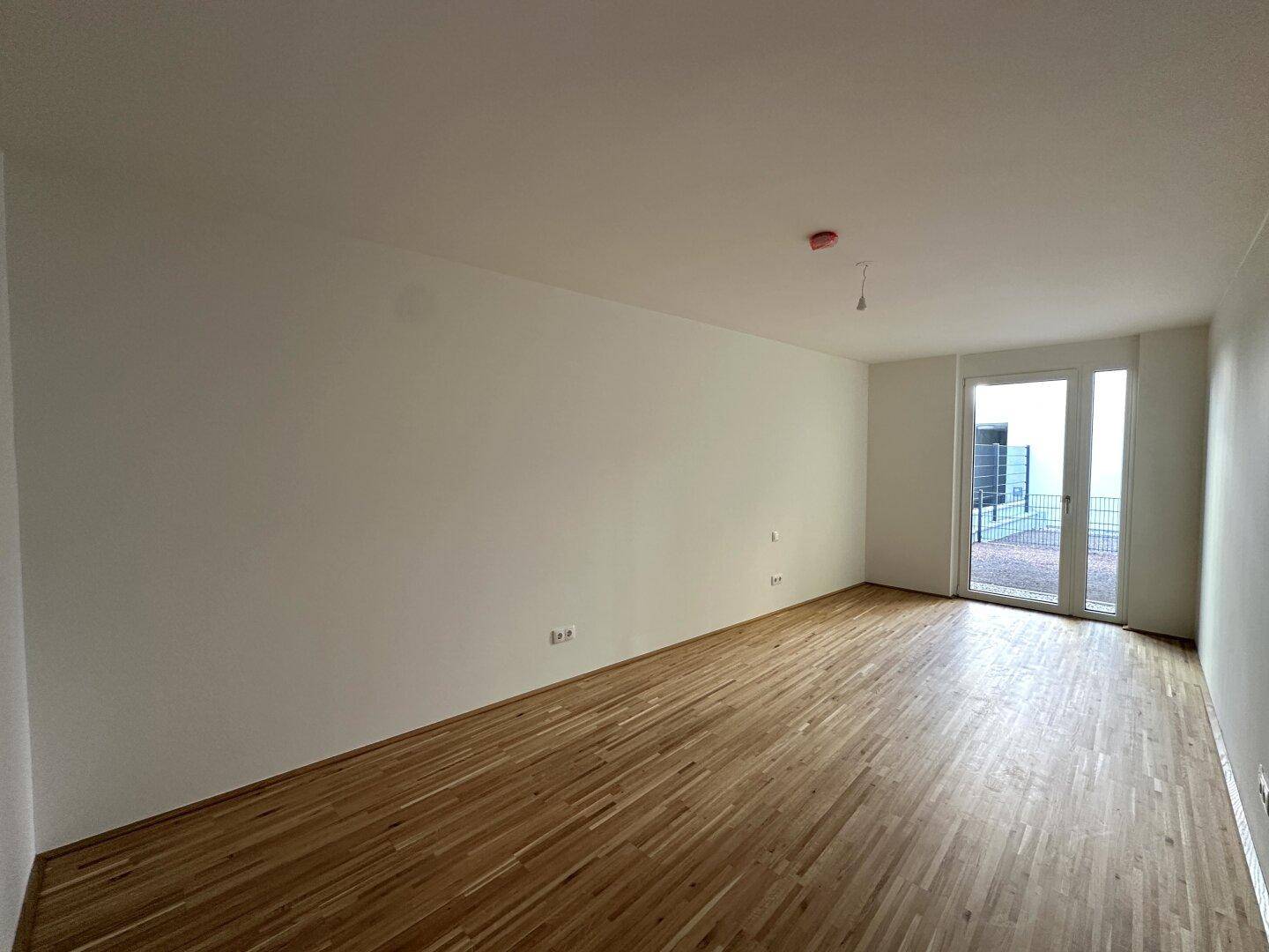 Geräumiger Wohnraum mit Parkettboden und direktem Zugang zur Außenterrasse.