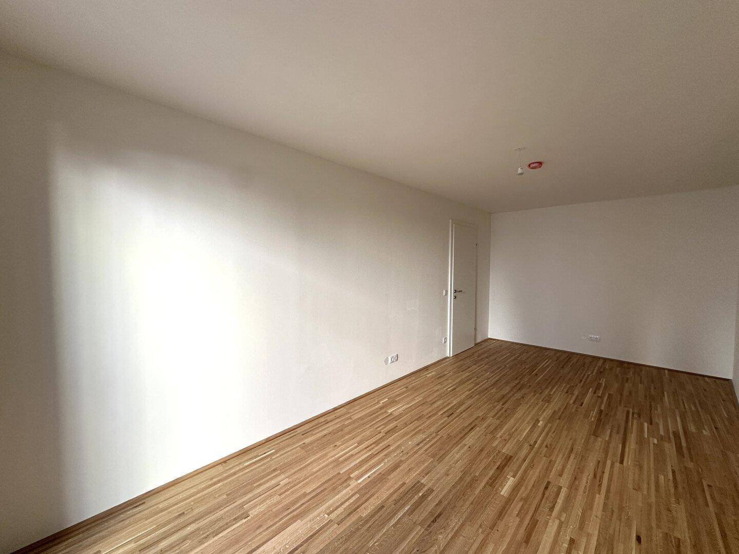 Leerer Wohnbereich mit Parkettboden und weiß gestrichenen Wänden, ideal für neue Bewohner.