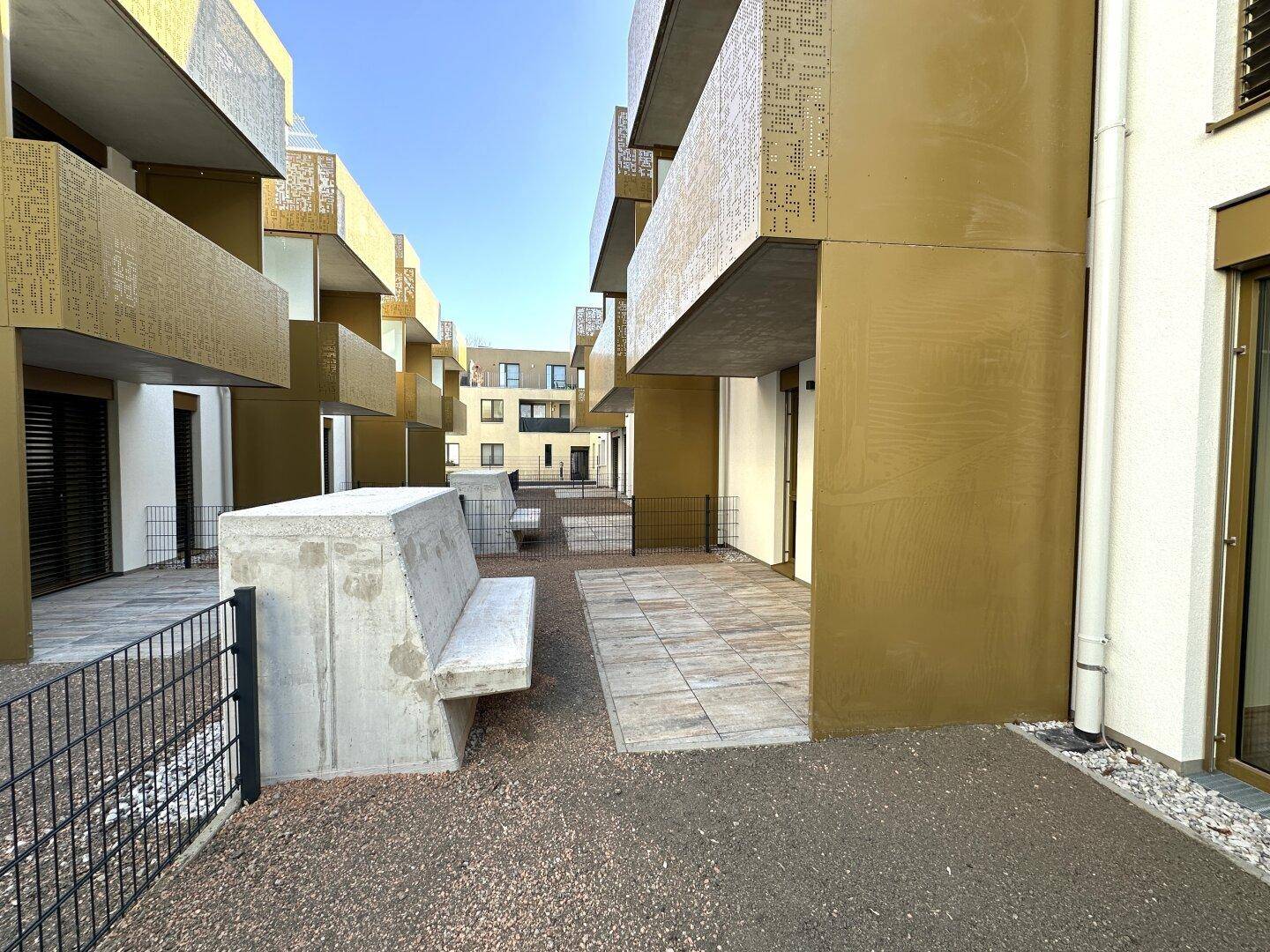 Außenbereich mit gepflasterter Terrasse und Gemeinschaftsflächen in einer modernen Wohnanlage.