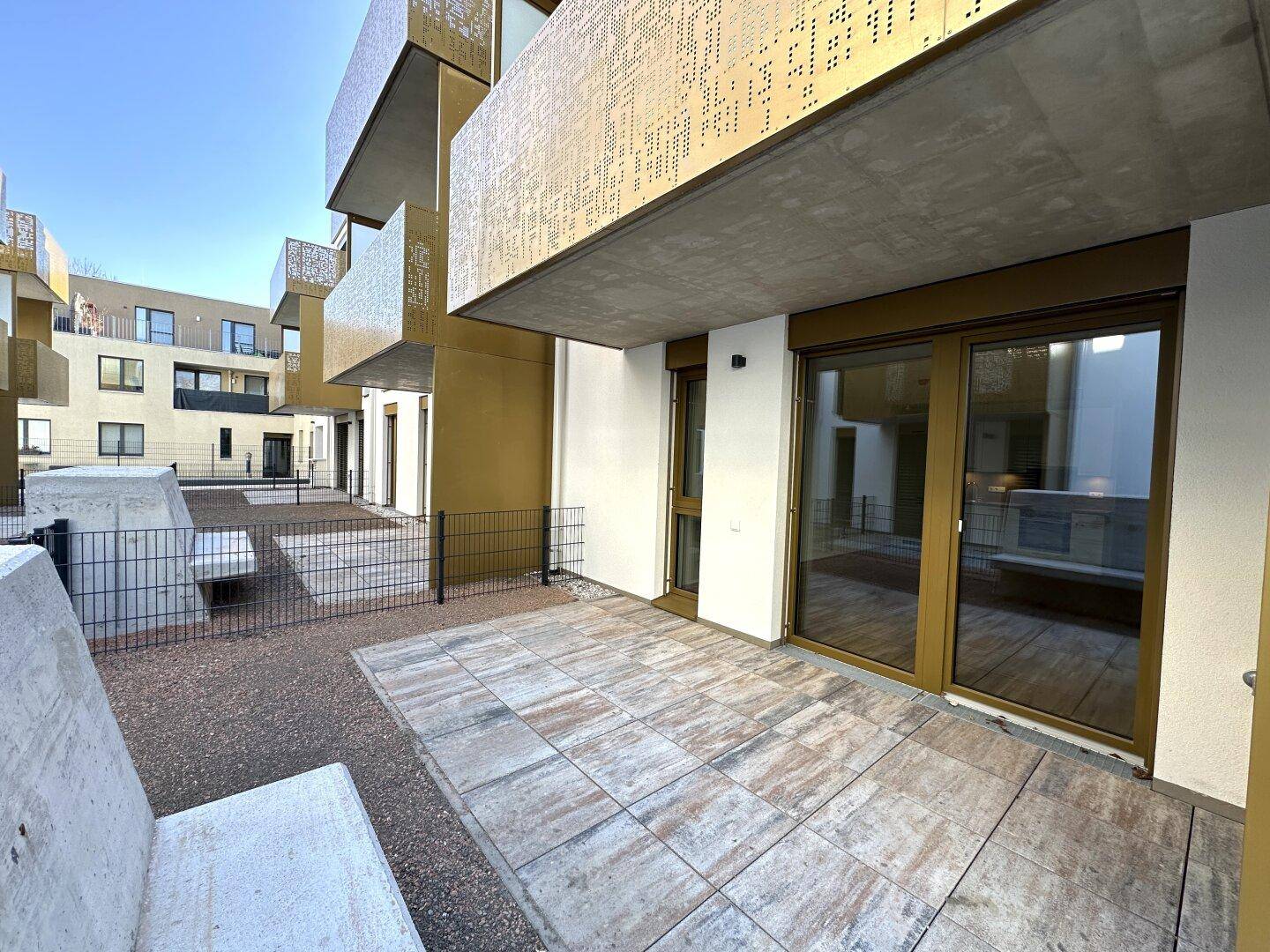 Sonniger Terrassenbereich mit Fliesenboden und Blick auf die moderne Wohnanlage.