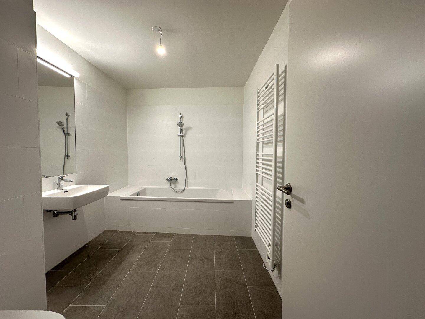 Modernes Badezimmer mit Badewanne, Waschbecken und beheiztem Handtuchhalter.