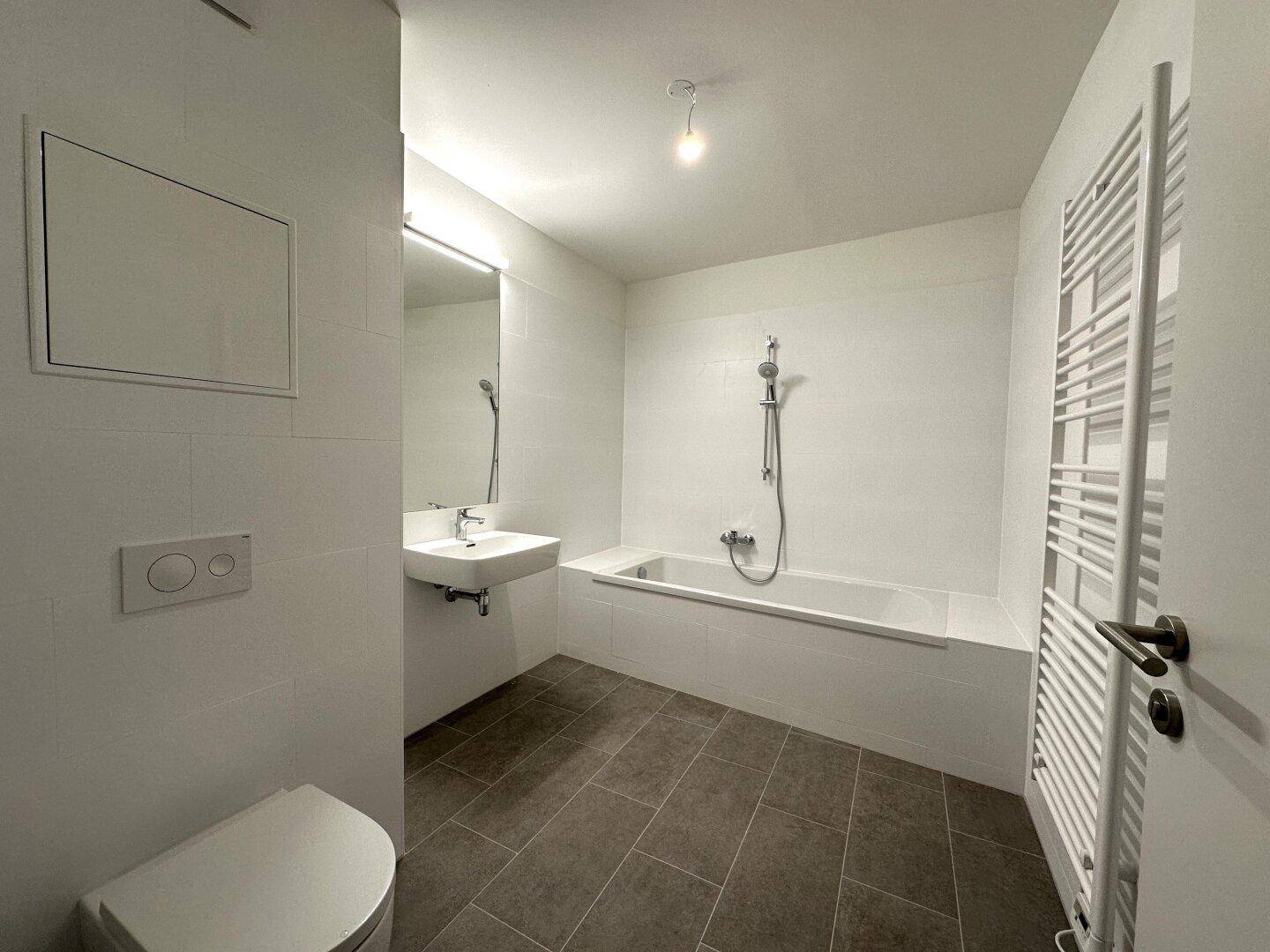 Helles Badezimmer mit Badewanne, WC, Waschbecken und großem Spiegel.