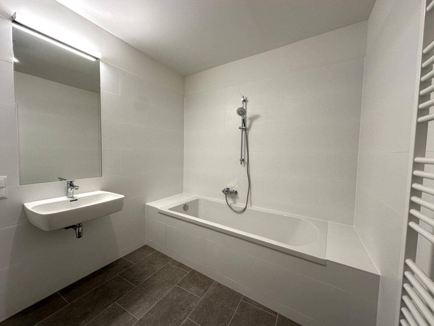 Zeitgemäßes Badezimmer mit Badewanne, elegantem Waschbecken und großem Wandspiegel.