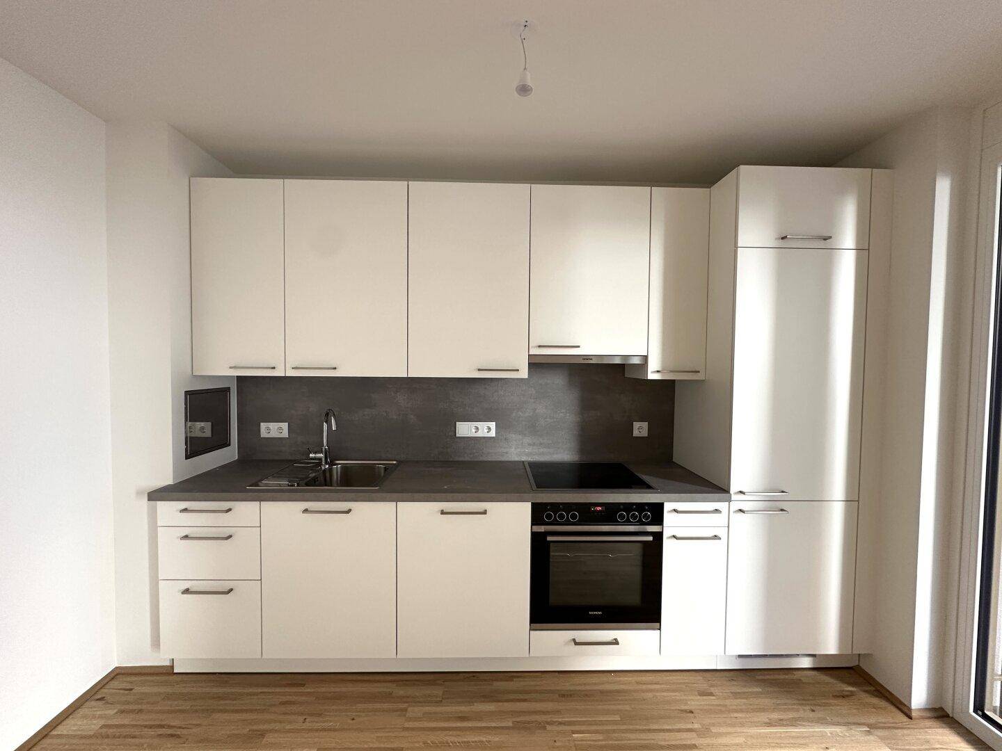 Moderne Einbauküche mit weißen Schränken, dunkler Arbeitsplatte und integrierten Geräten.