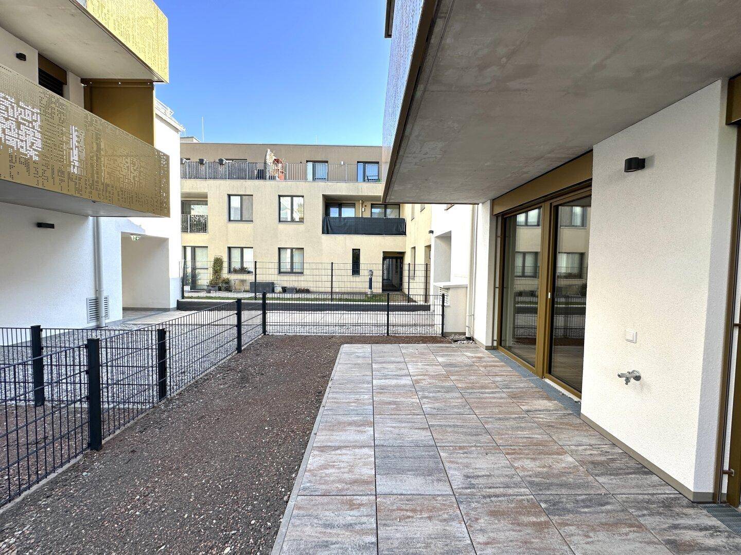 Gepflasterte Terrasse im Erdgeschoss mit Blick auf den Innenhof des Neubaus.