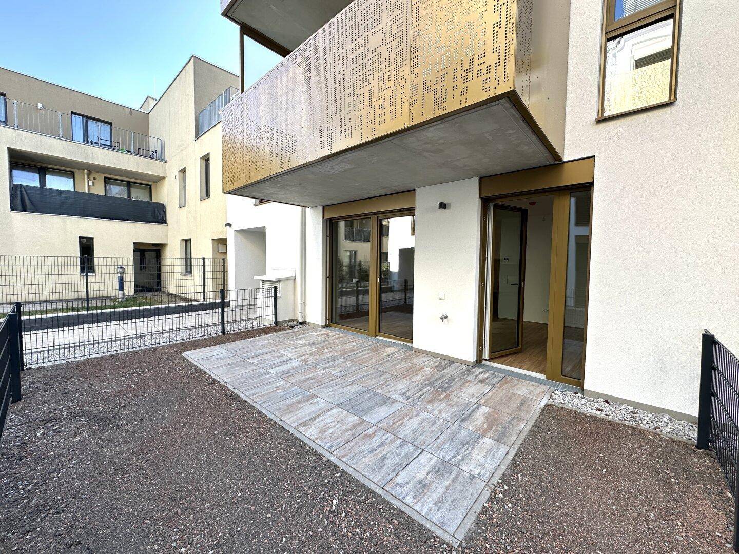 Geräumige, gepflasterte Terrasse vor der modernen Fassade eines Neubaukomplexes.