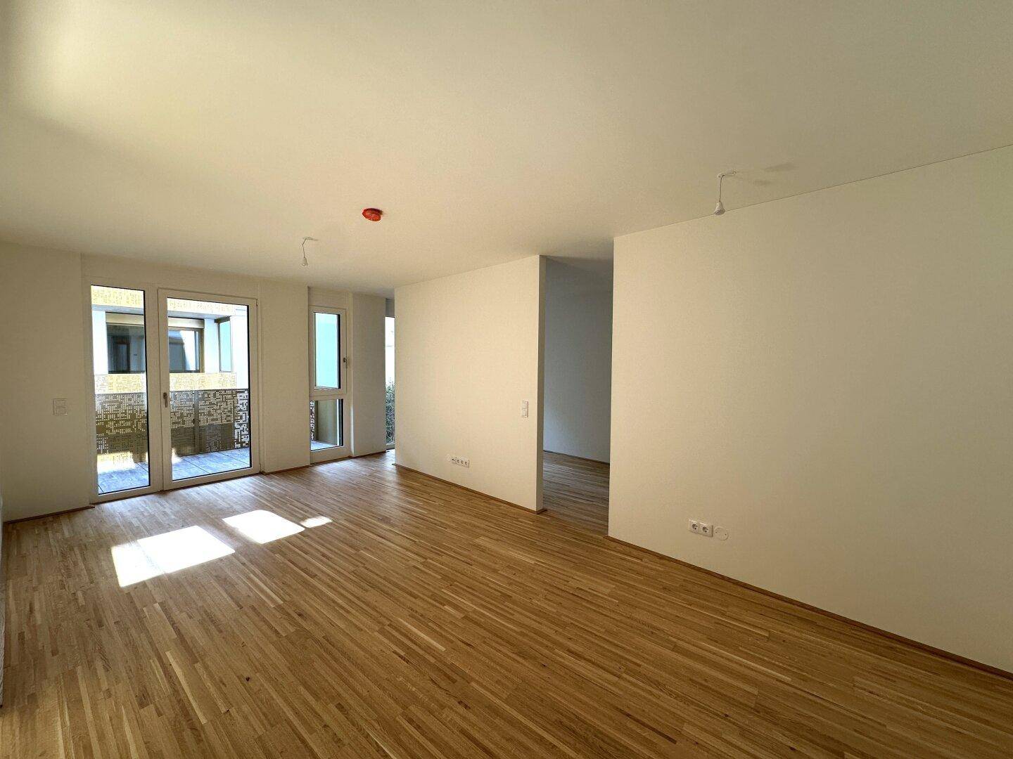 Lichtdurchflutetes Wohnzimmer mit Holzboden und großen Fenstern, die Zugang zum Außenbereich bieten.