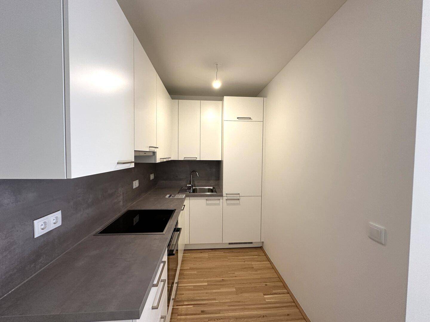 Moderne Küchenzeile mit weißen Schränken, dunkler Arbeitsplatte und integriertem Kochfeld.