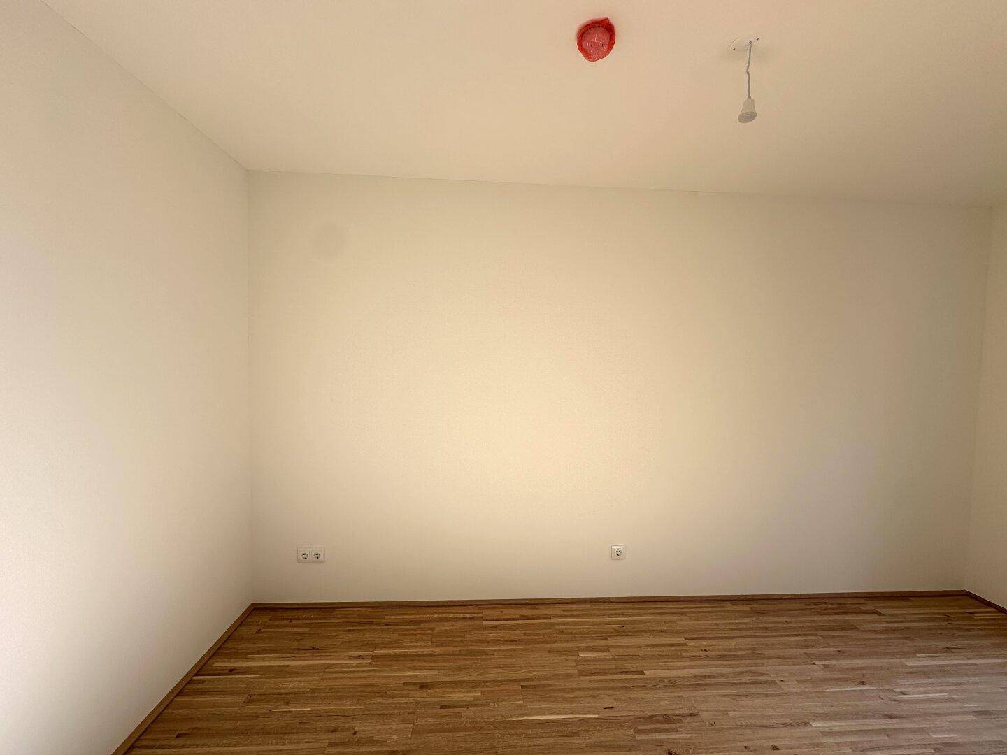 Leeres Zimmer mit Parkettboden und weißen Wänden, bereit für individuelle Einrichtung.