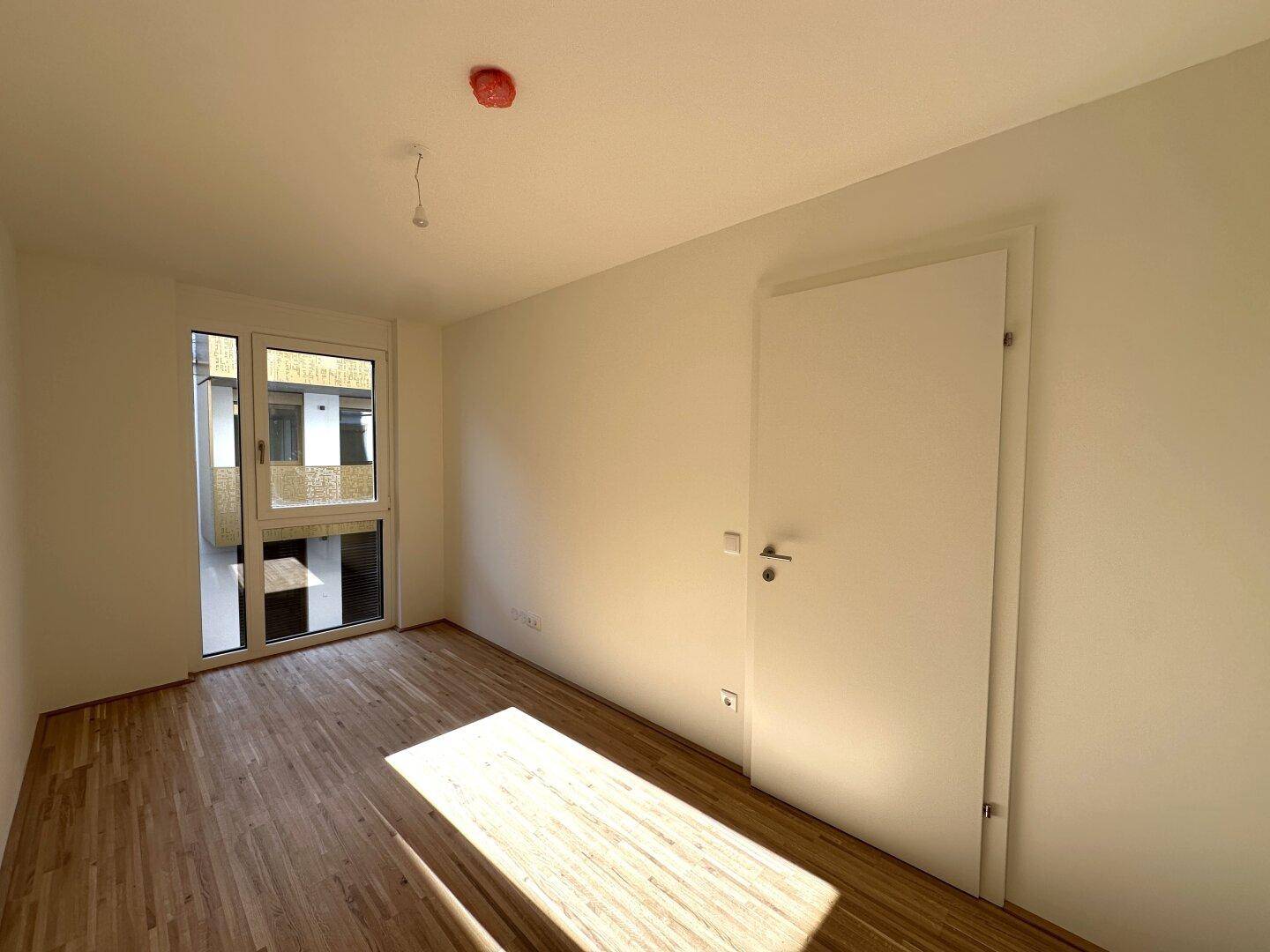 Helles Zimmer mit Parkettboden und Fenster, das viel natürliches Licht in den Raum bringt.