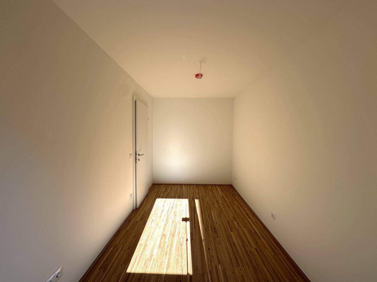 Geräumiges Zimmer mit Parkettboden und weiß gestrichenen Wänden, ideal als Schlaf- oder Arbeitszimmer.