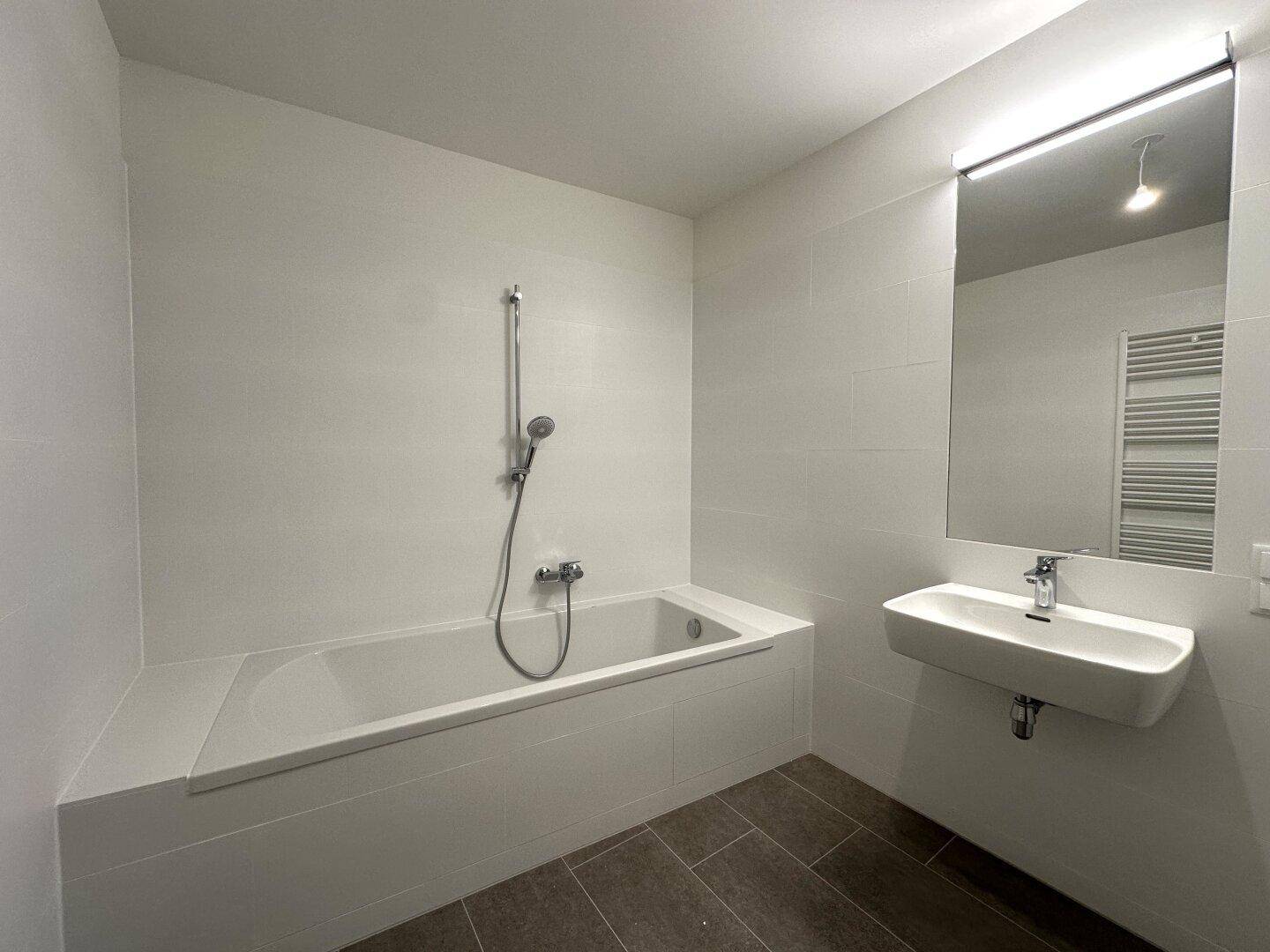 Zeitgemäßes Badezimmer mit Badewanne, elegantem Waschbecken und großem Spiegel mit Beleuchtung.