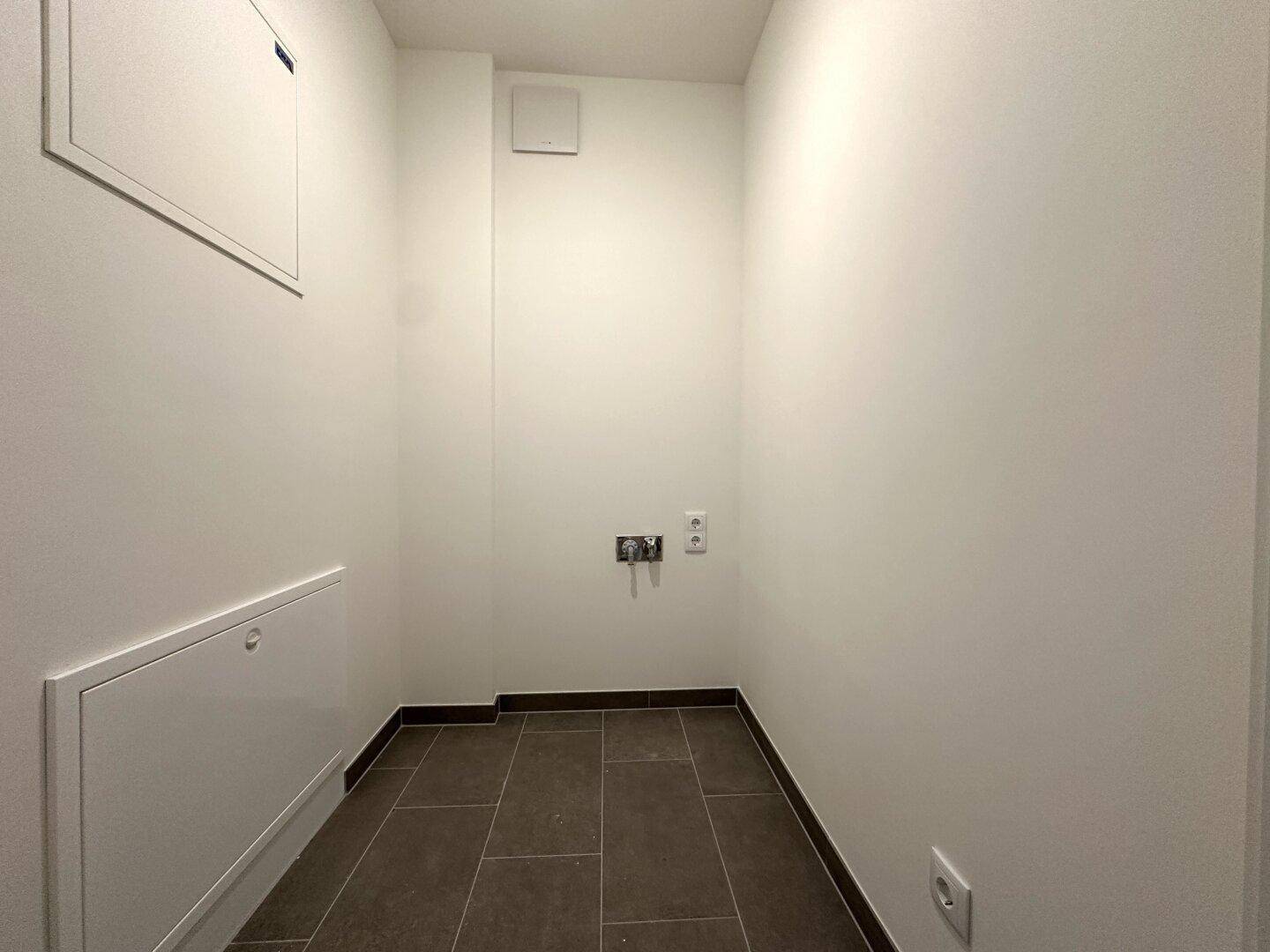 Praktischer Abstellraum mit Fliesenboden und Anschlüssen für Waschmaschine und Trockner.