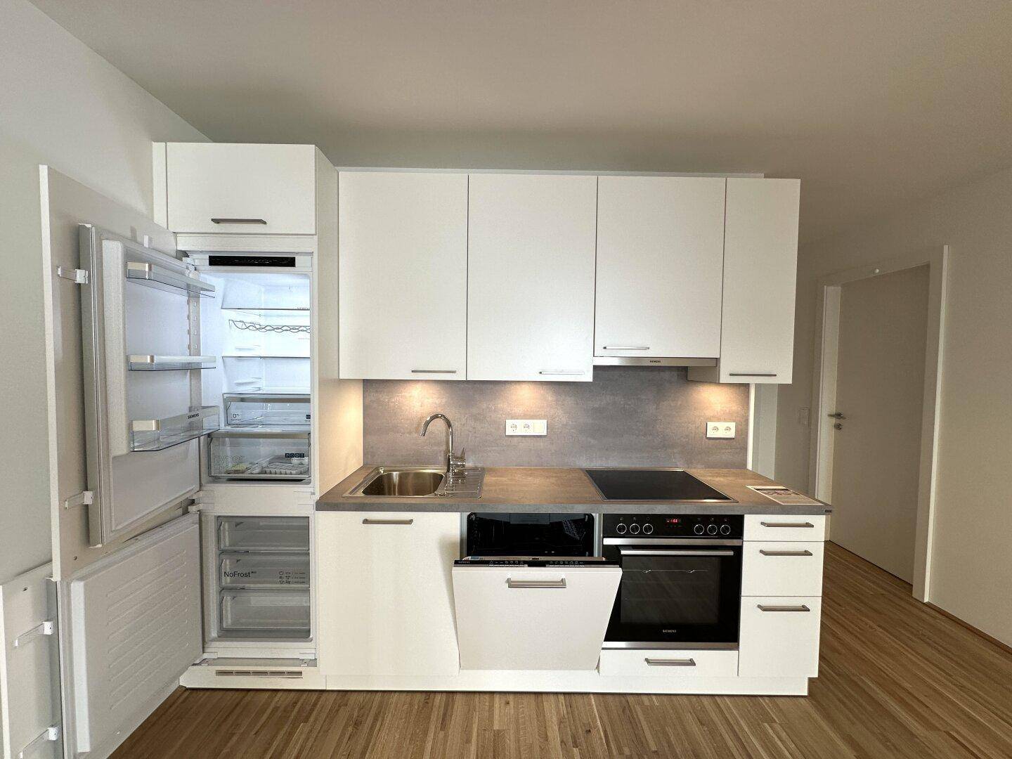 Voll ausgestattete, weiße Einbauküche mit Kühlschrank, Geschirrspüler und Backofen.