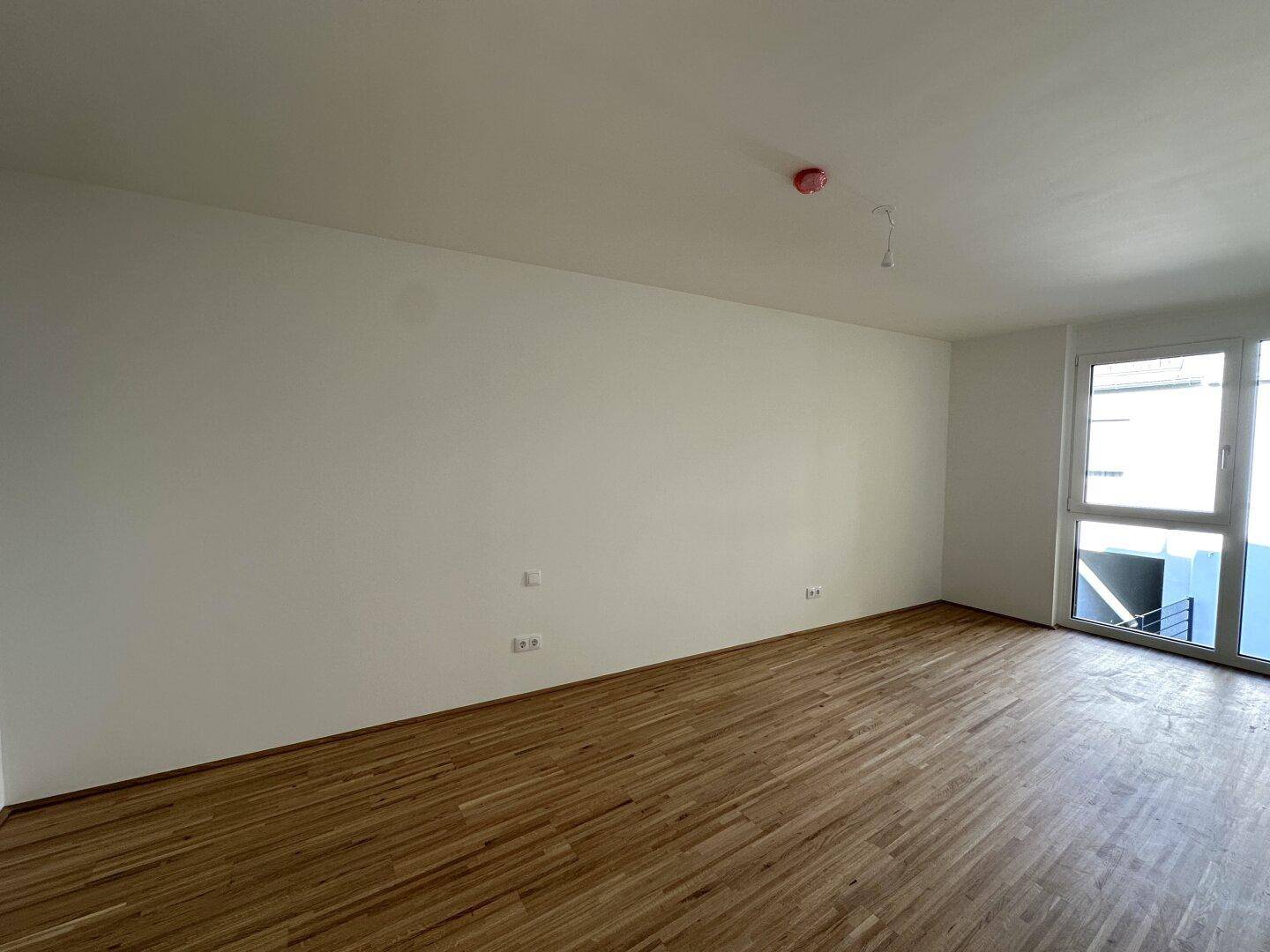 Heller Raum mit Holzboden und einem Fenster, das Tageslicht hereinlässt.