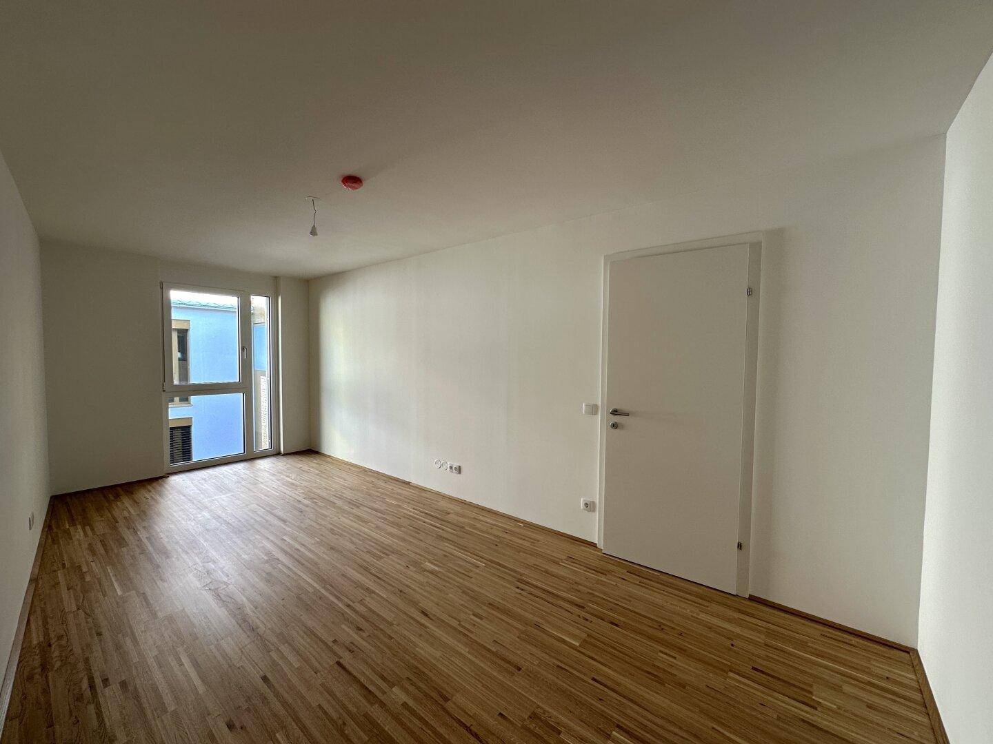 Geräumiger, heller Raum mit Holzboden und einer Tür, die zu einem anderen Bereich führt.