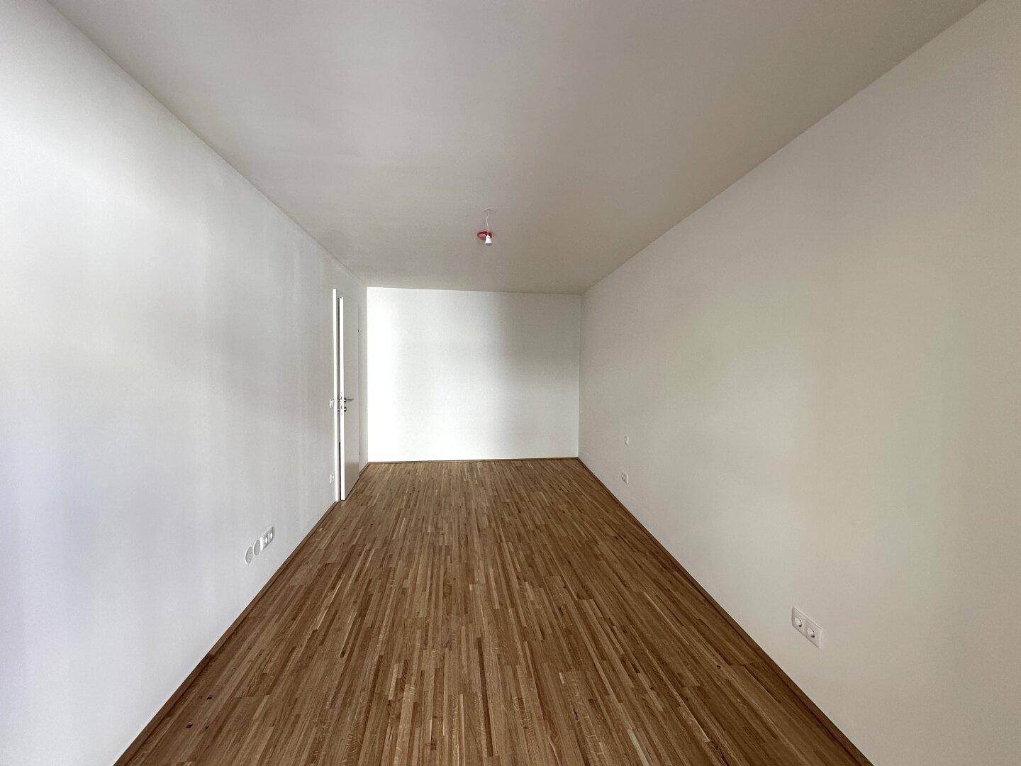 Leerer Raum mit Holzboden und weißen Wänden, ideal für ein Schlafzimmer oder Büro.