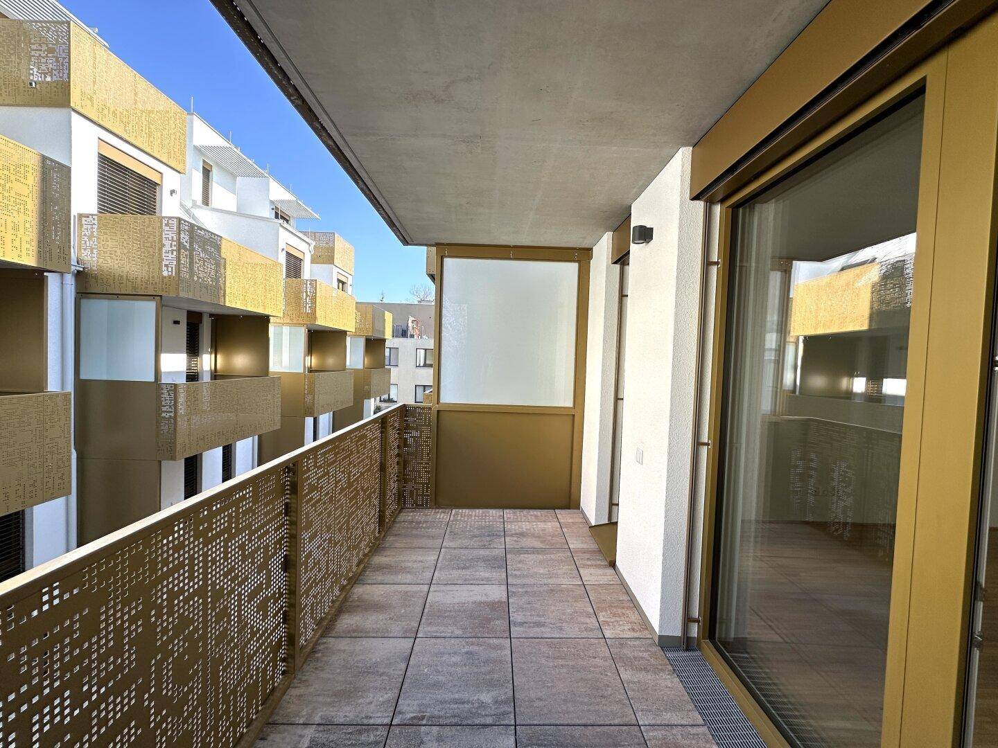 Moderner Balkon mit Fliesenboden und dekorativem Metallgeländer, sonnig.