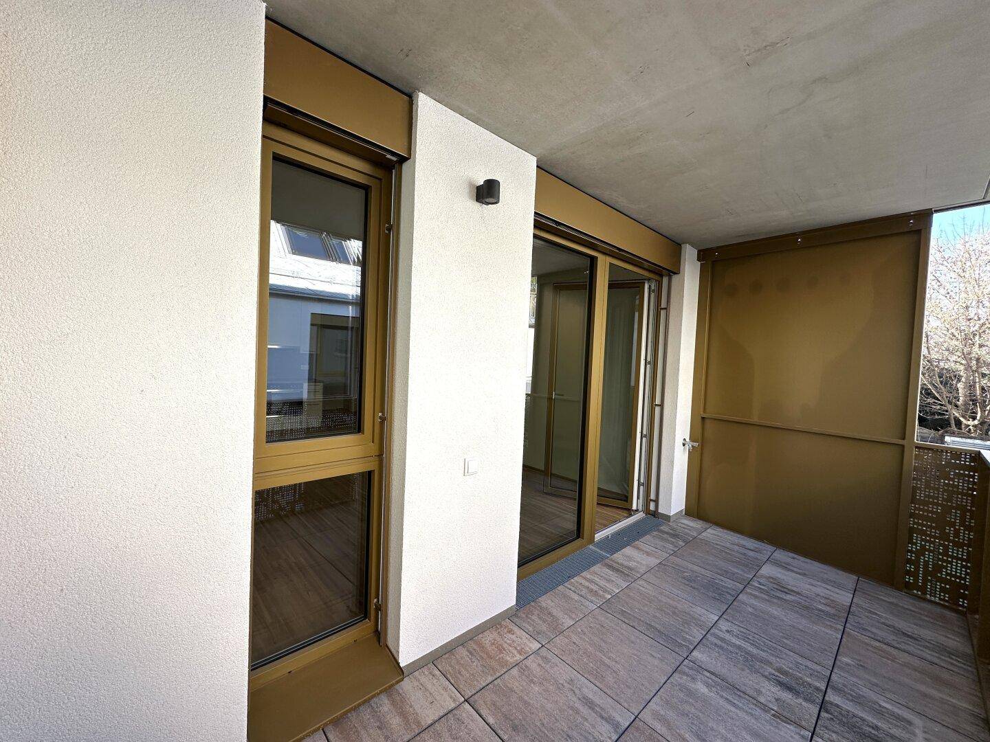 Geräumiger Balkon mit Fliesenboden und Zugang zum Innenbereich durch eine Glastür.