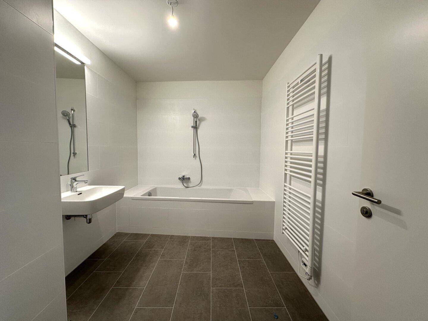 Modernes Badezimmer mit Badewanne, Waschbecken und beheiztem Handtuchhalter.