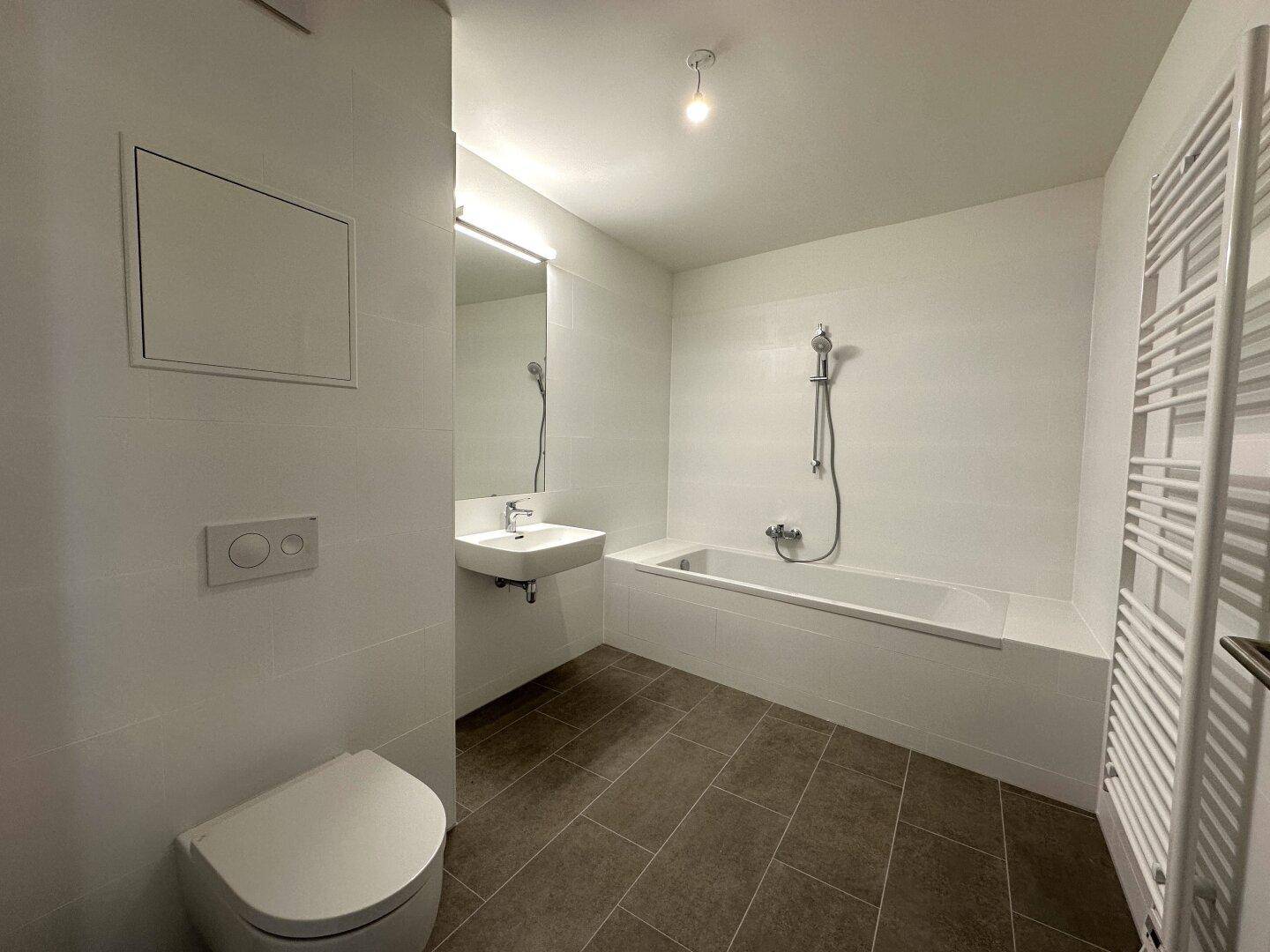Modernes Badezimmer mit Badewanne, Toilette, Waschbecken und Fliesenboden.