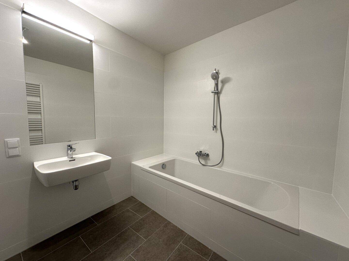Helles Badezimmer mit Badewanne, modernem Waschbecken und großem Spiegel.