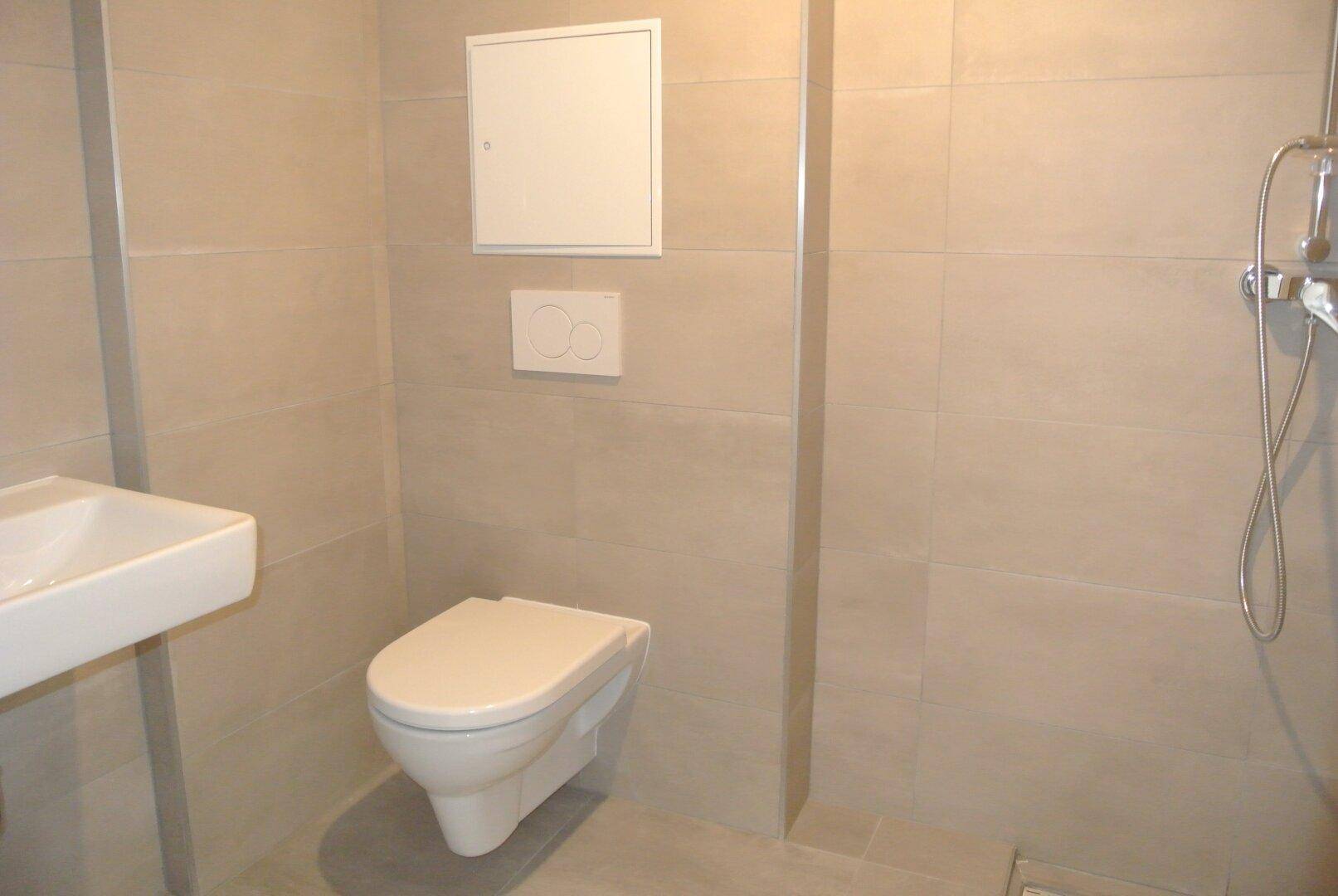 Modernes Badezimmer mit wandhängendem WC, Waschbecken und Duschbereich, komplett gefliest.