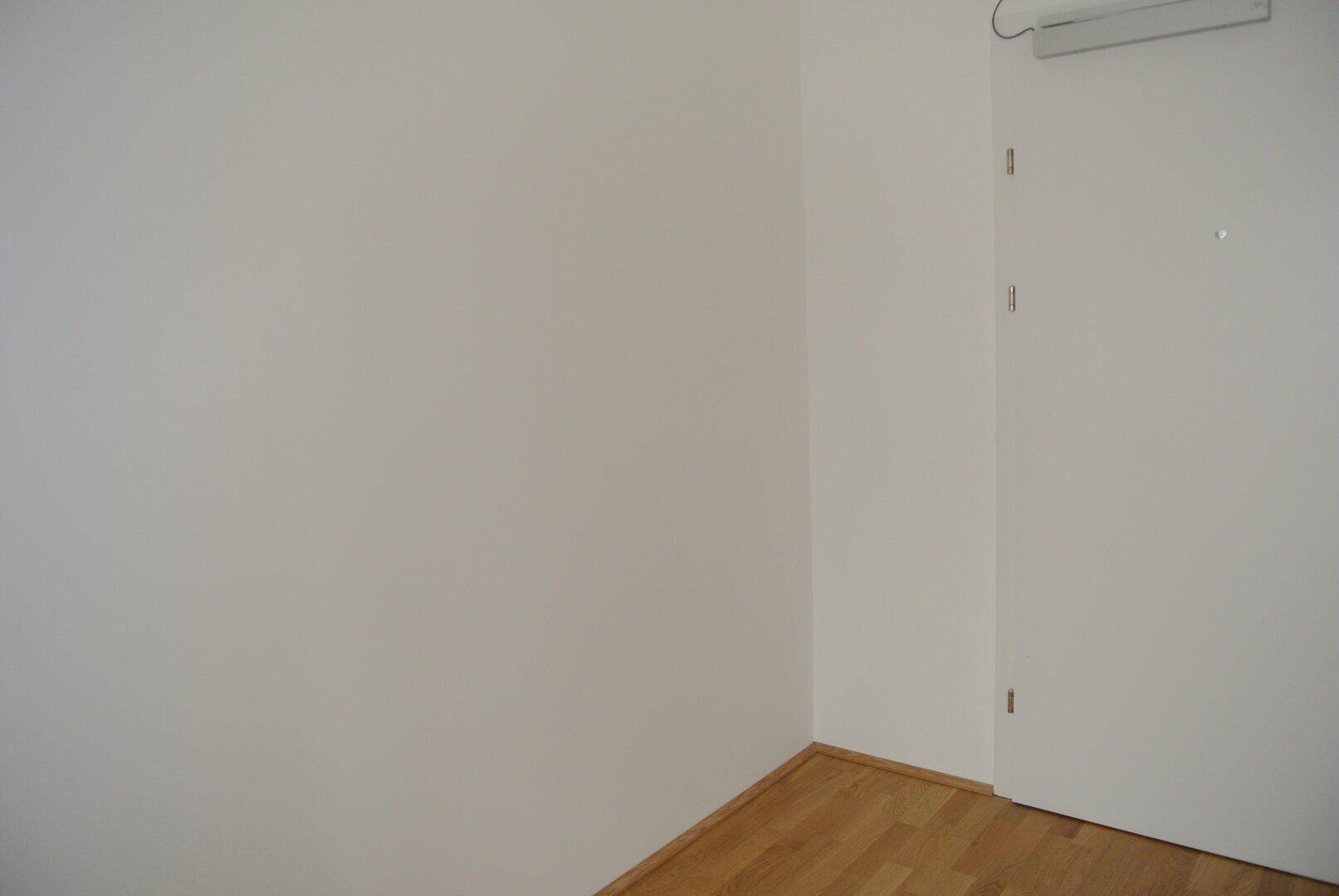Heller Flurbereich mit weißer Tür und Parkettboden in einem modernen Gebäude.