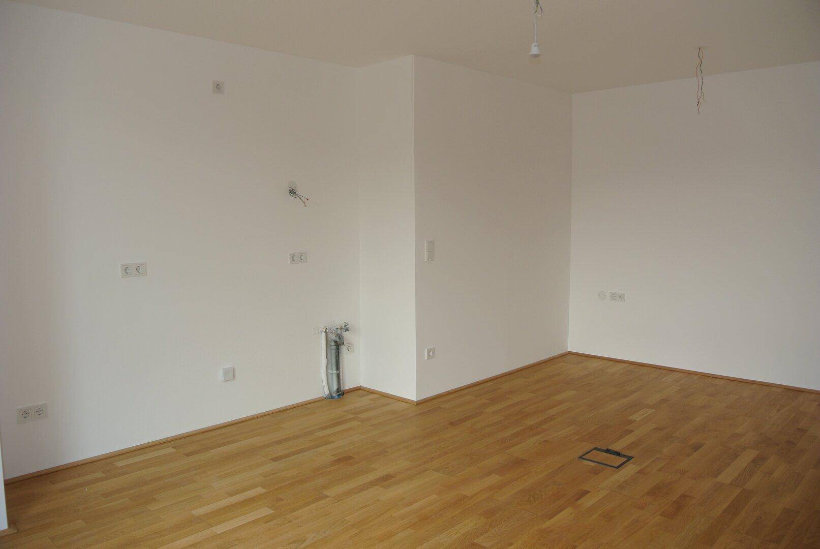 Leerer Raum mit hellem Holzparkettboden und weißen Wänden, vorbereitet für Installationen.