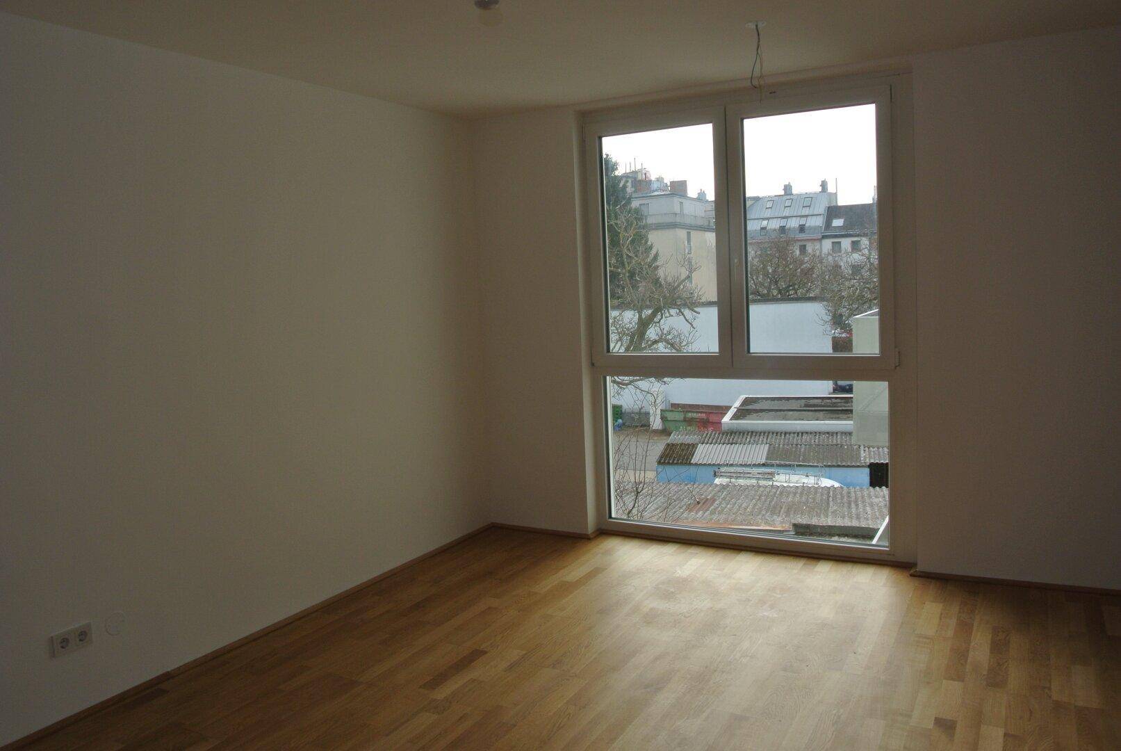 Heller Raum mit Parkettboden und großem Fenster mit Blick auf die Umgebung.
