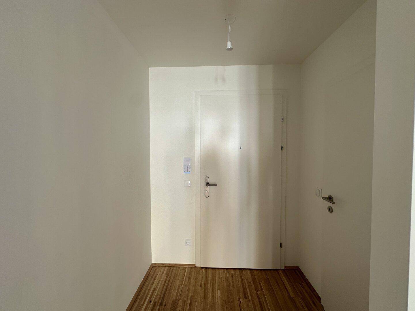 Heller Eingangsbereich mit Holzboden und weißer Eingangstür, einladend gestaltet.