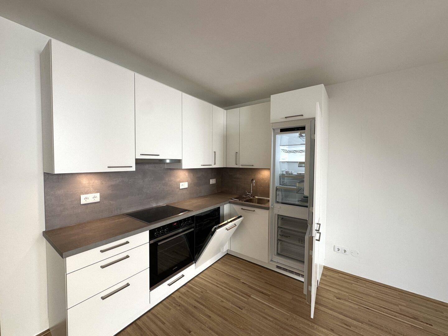 Weiße Einbauküche mit integriertem Geschirrspüler und Kühlschrank, ideal für kompaktes Wohnen.