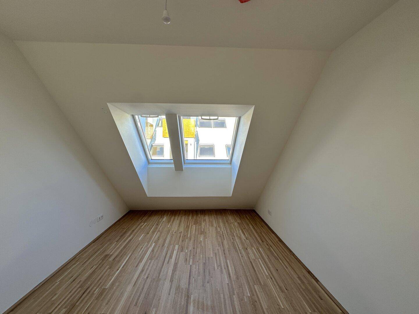 Helles Zimmer im Dachgeschoss mit Holzboden und großem Dachfenster für viel Tageslicht.