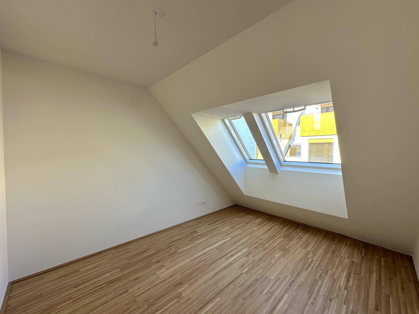 Dachgeschosszimmer mit Holzboden und schrägen Wänden, beleuchtet durch ein großes Dachfenster.