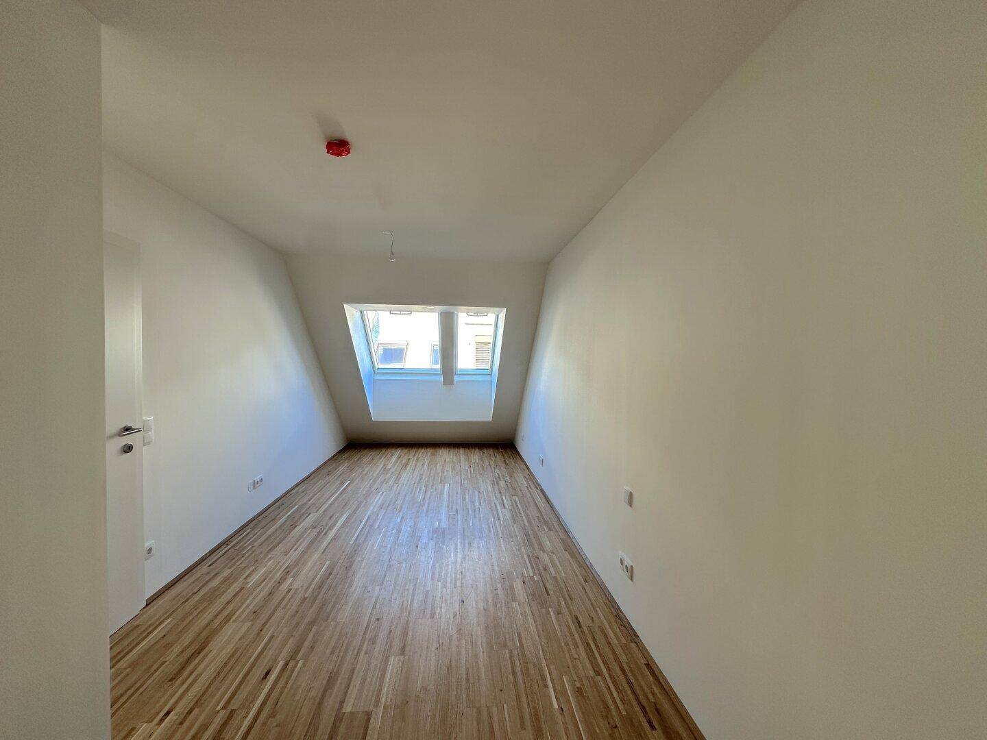 Gemütliches Zimmer im Dachgeschoss mit Holzboden und einem Fenster in der Dachschräge.