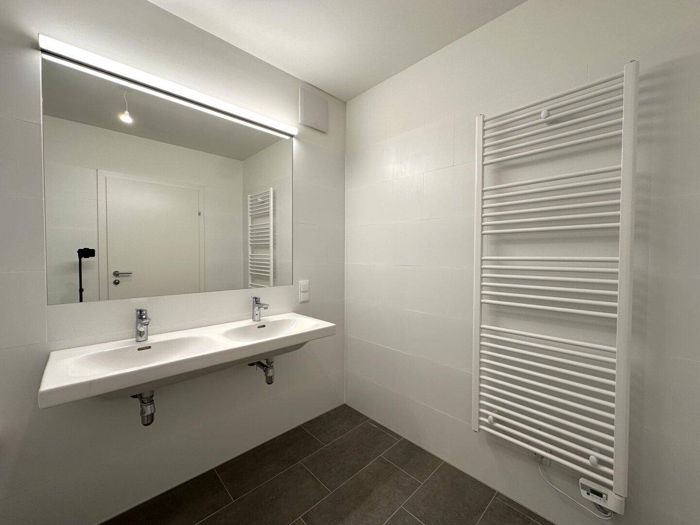 Helles Badezimmer mit Doppelwaschbecken, großem Spiegel und praktischem Handtuchheizkörper.