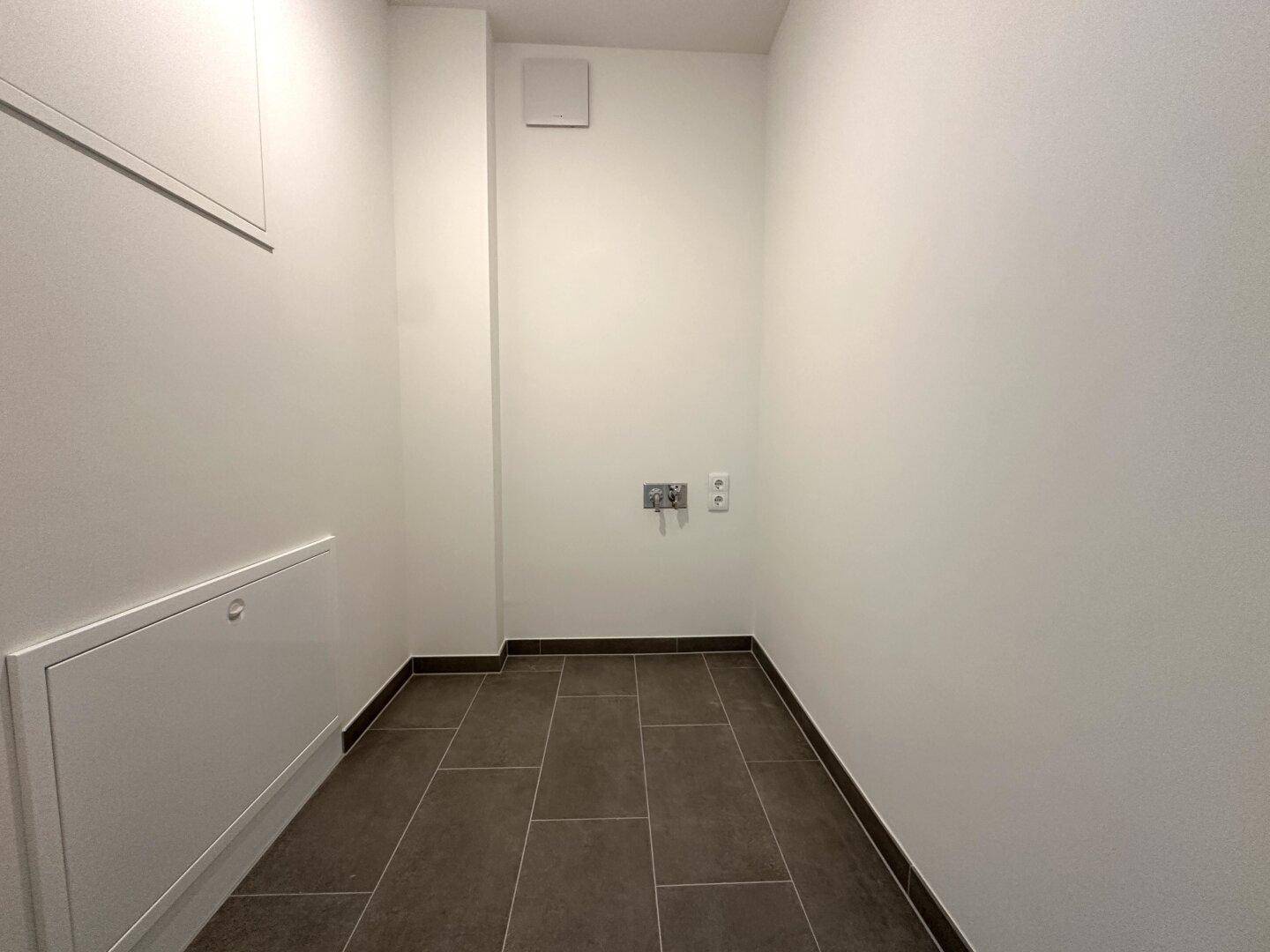 Praktischer Hauswirtschaftsraum mit Fliesenboden und Anschlüssen für Waschmaschine und Trockner.
