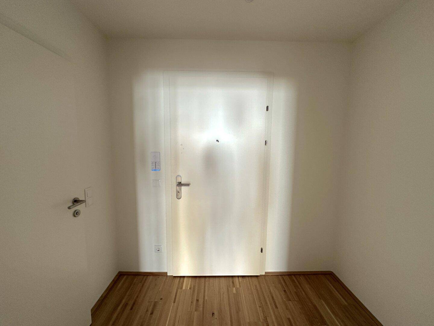 Eingangsbereich mit Holzboden und weißer Tür, bietet Zugang zu den Wohnräumen.