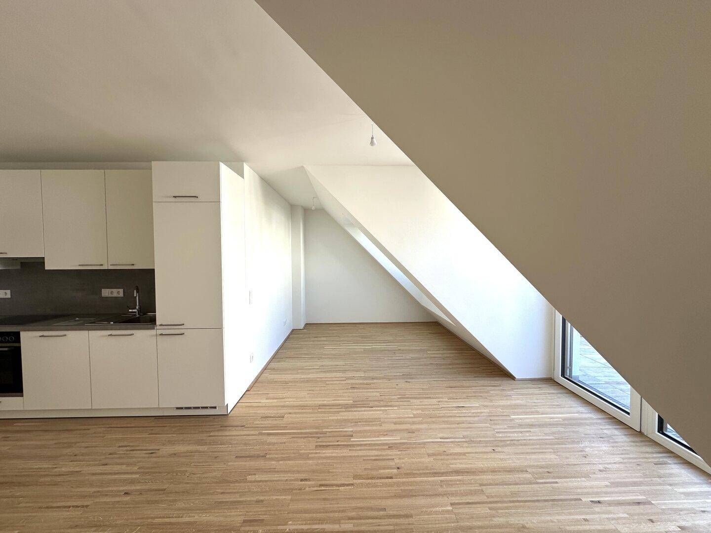 Lichtdurchfluteter Wohnbereich mit Holzboden, schrägen Wänden und großem Fenster.