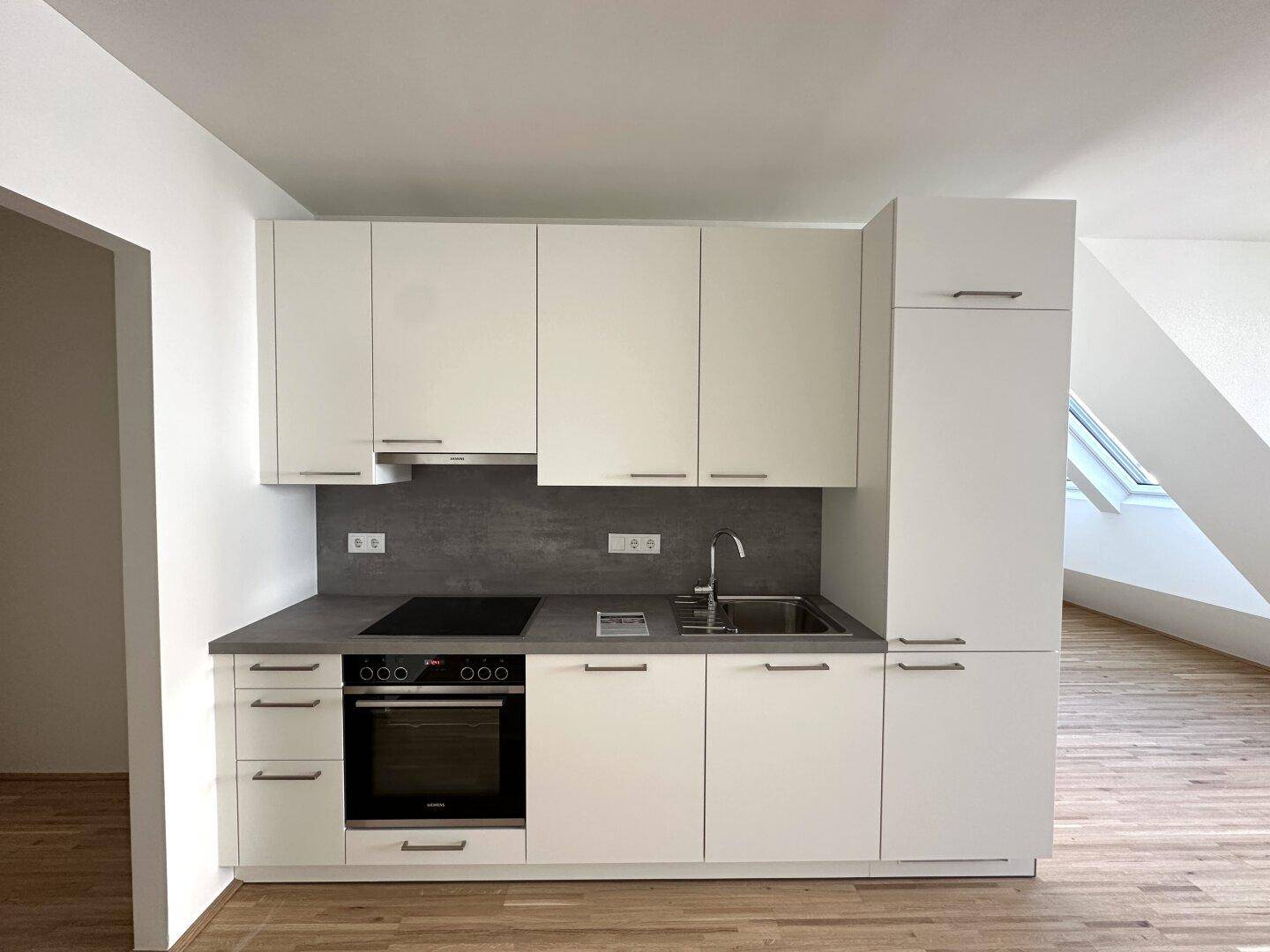 Moderne Einbauküche mit weißen Schränken, dunkler Arbeitsplatte und integrierten Geräten.