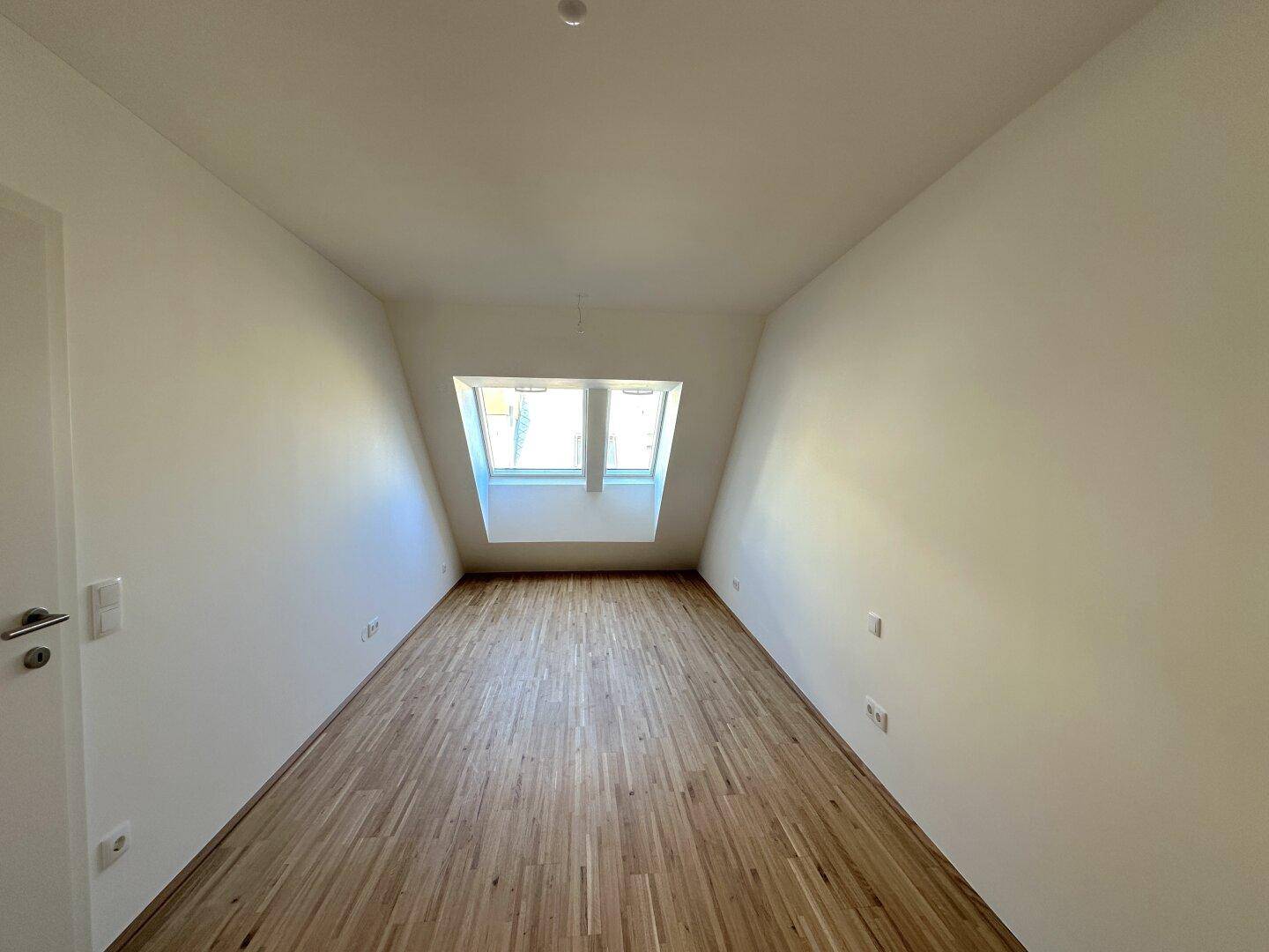 Helles Schlafzimmer im Dachgeschoss mit Parkettboden und großem Dachfenster.