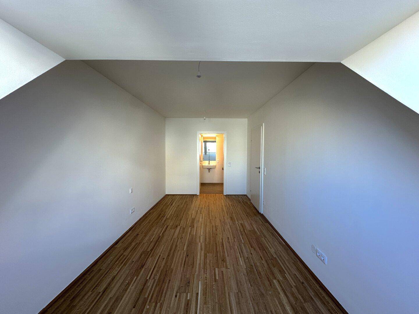 Geräumiges Schlafzimmer mit Parkettboden und Zugang zum Badezimmer.