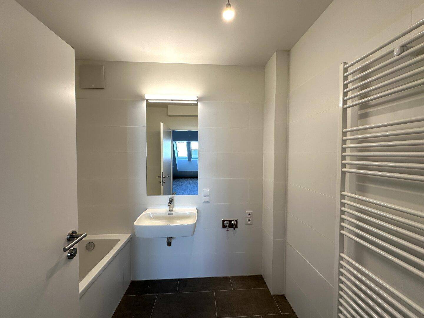Modernes Badezimmer mit Badewanne, Einzelwaschbecken und beheiztem Handtuchhalter.
