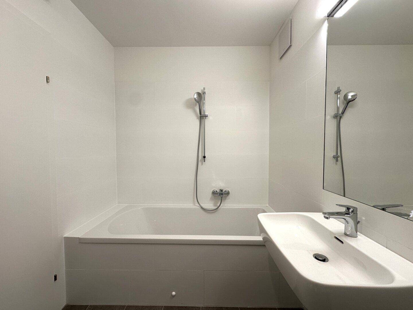 Helles Badezimmer mit Badewanne, Duschfunktion und modernem Waschbecken.