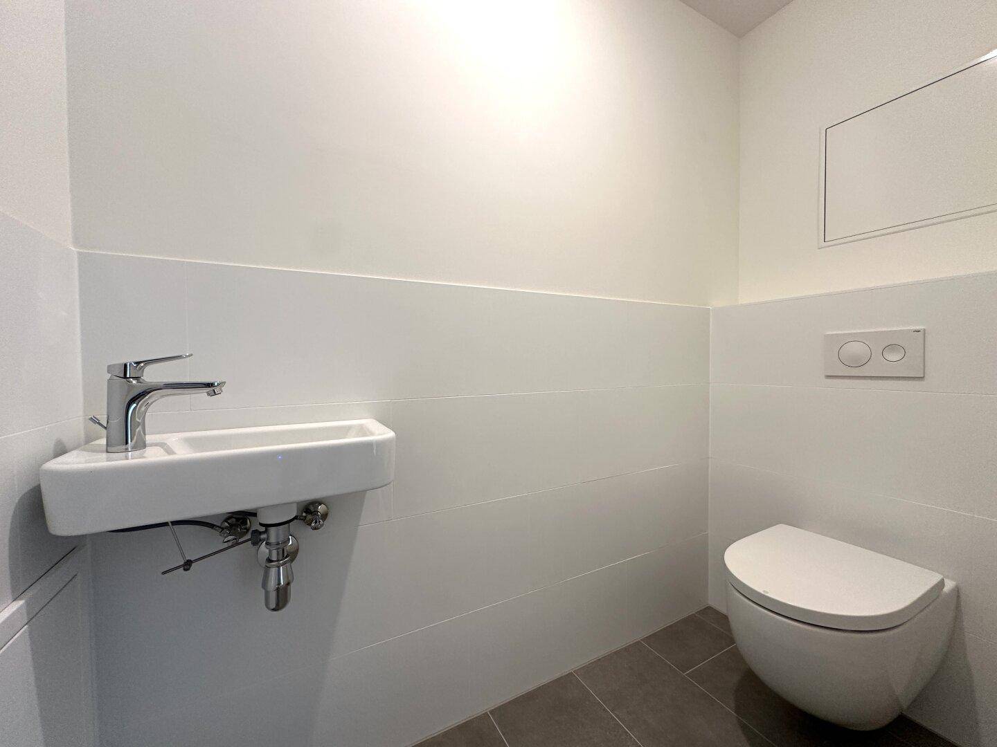 Sauberes Gäste-WC mit minimalistischem Design, wandhängender Toilette und Waschbecken.