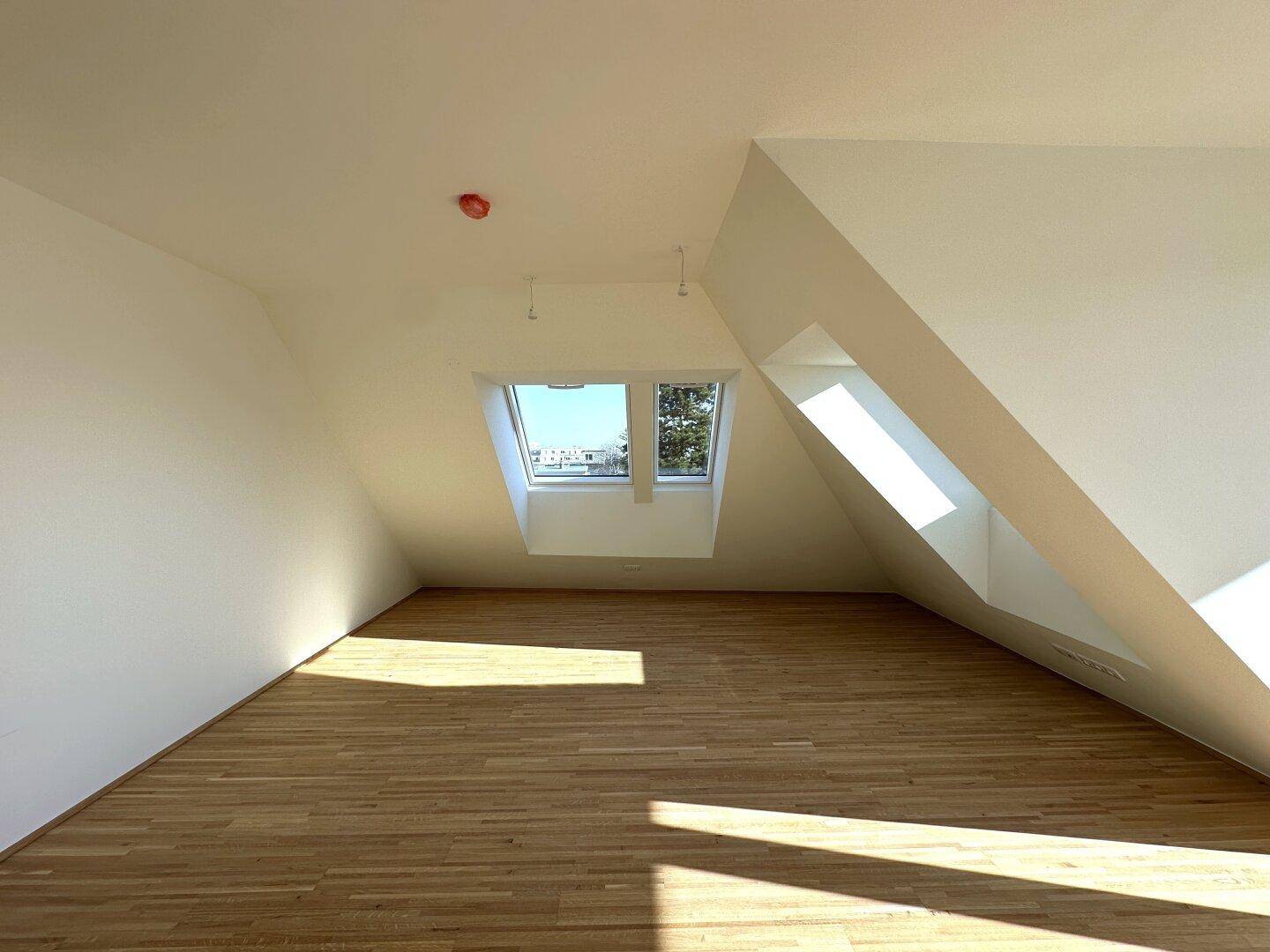 Lichtdurchfluteter Wohnraum mit Parkettboden und schrägen Dachfenstern, ideal für ein gemütliches Zuhause.