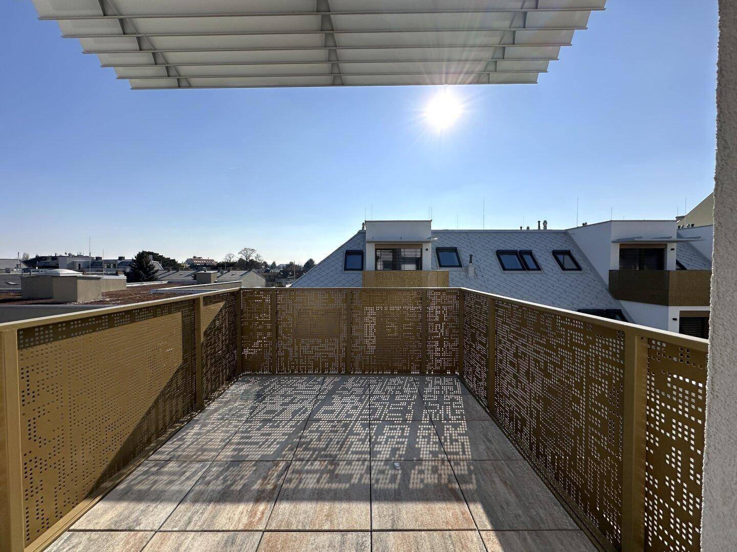 Sonnige Dachterrasse mit modernen perforierten Geländern und einem weiten Blick über die Stadt.